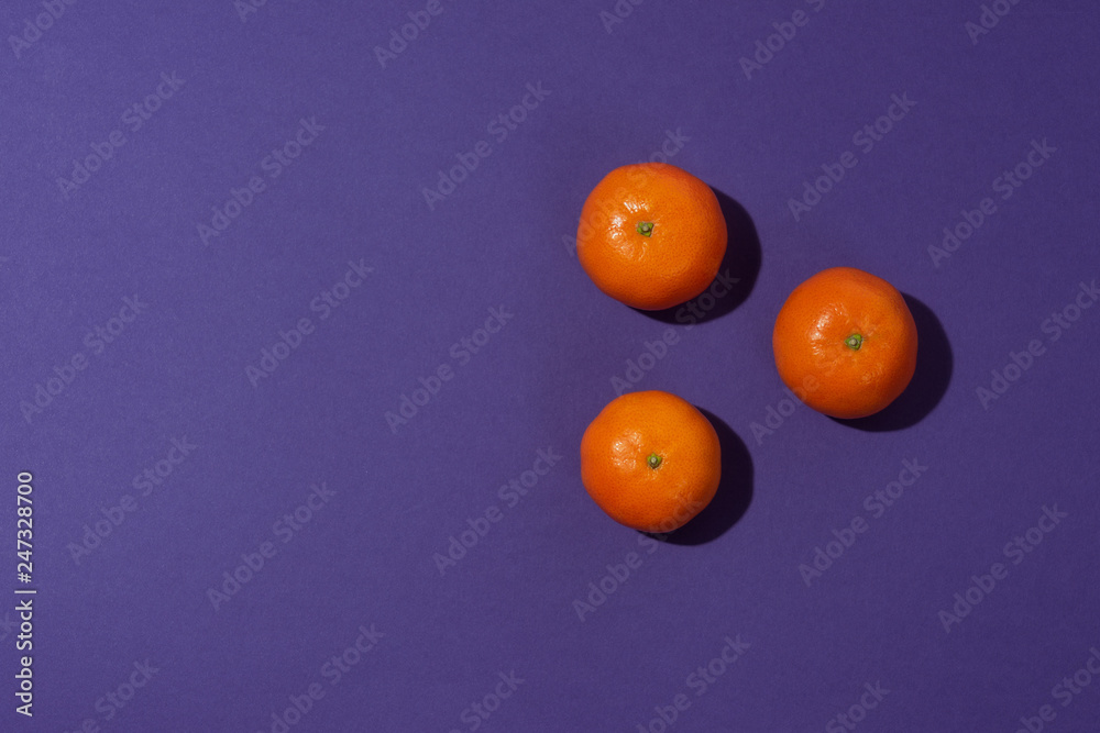 Three tangerines in the shape of a triangle on purple background captured with hard light. View from above and place for copy space. Three tangerines in the shape of a triangle on purple background captured with hard light. View from above and place for copy space.