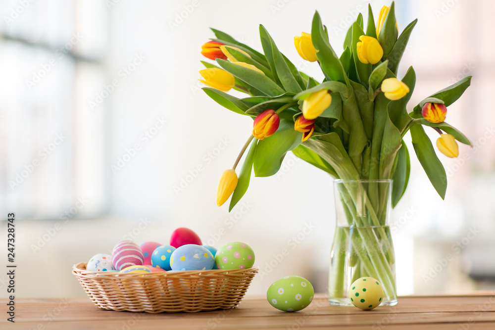 Obraz premium easter, holidays, tradition and object concept - colored eggs in basket and tulip flowers at home