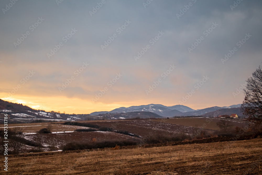 Winter sunset with mountains and meadows in the background and little bits of snow