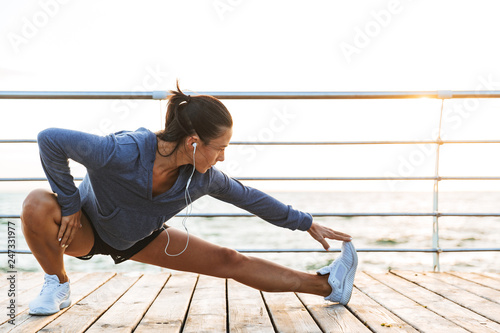 Fitness woman make stretching exercises at the beach outdoors listening music with earphones.