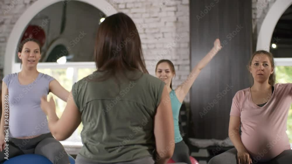 Group of three pregnant women sitting on exercise balls and doing stretching and breathing exercises before yoga workout Group of three pregnant women sitting on exercise balls and doing stretching and breathing exercises before yoga workout