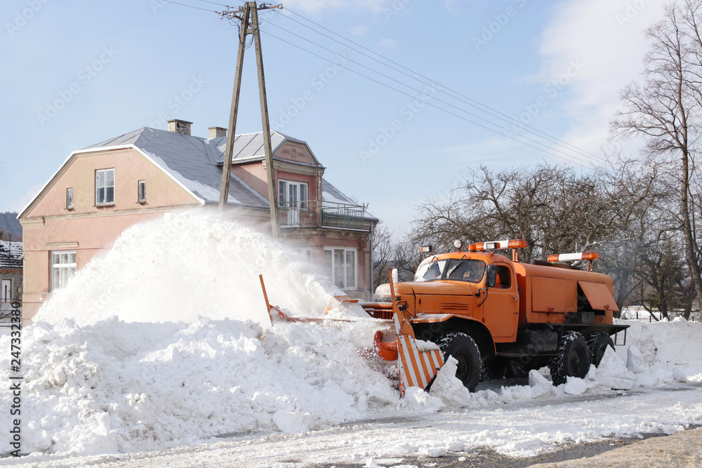 A large car with a plow clears the road from snow. Orange cargo special equipment is struggling with the elements in winter. Removing the effects of the snowstorm. Difficulties in traffic.Frozen water A large car with a plow clears the road from snow. Orange cargo special equipment is struggling with the elements in winter. Removing the effects of the snowstorm. Difficulties in traffic.Frozen water