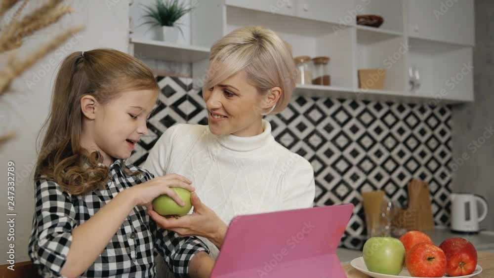Mother giving green apple to daughter in kitchen.