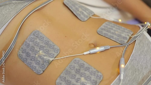 Close-up of medical electrodes biostimulating apparatus for body massage on the stomach of a young woman. Attractive young woman in beauty medical spa center anti-cellulite electrostimulation therapy.
