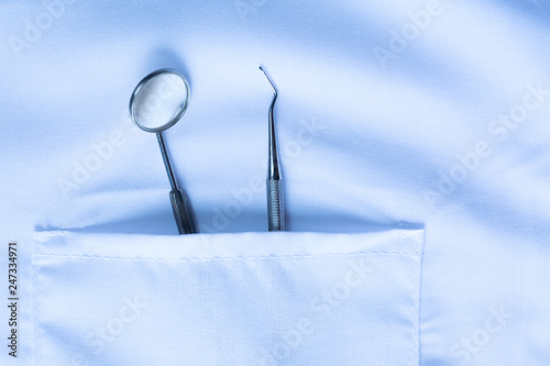 Closeup of dental tool and a mirror in white medical uniform pocket. Blue toned. Dental hygiene concept.