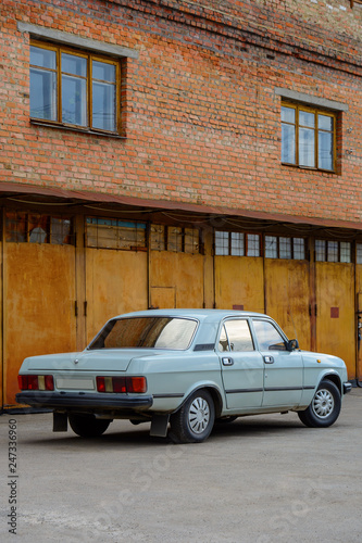 Photo of old car standing before rusty gate of building