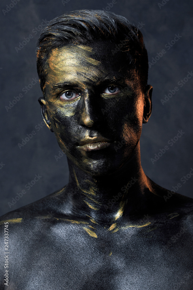 a man in black make-up with gold. portrait of a guy in dark paint with gold. Artistic portrait photography a man in black make-up with gold. portrait of a guy in dark paint with gold. Artistic portrait photography