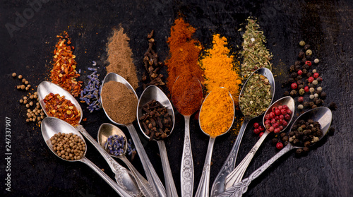 Different spices in spoons on a dark wooden table