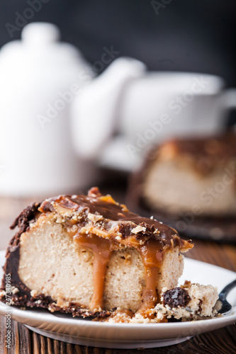Close up view of a piece of peanut butter chocolate caramel cheesecake pie and cup of coffee on wooden background with a coffee pot and cheesecake in the background. A Sweet Coffee Break concept 