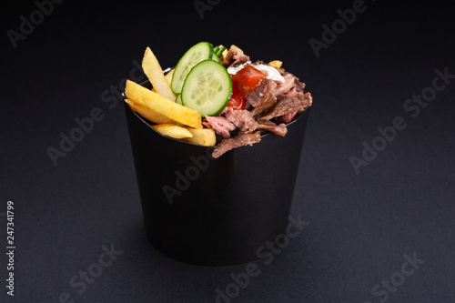 cooked shawarma plate with beef, french fries, vegetables and sauce close-up on a black background. horizontal top view from above