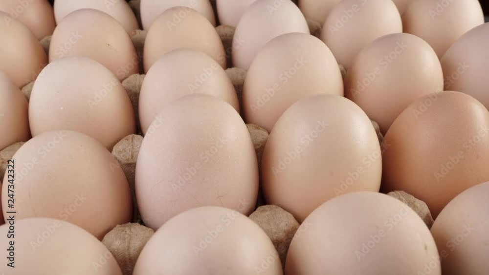 Fresh uncooked large chicken eggs in a paper box rotate on a stand. Fresh uncooked large chicken eggs in a paper box rotate on a stand.