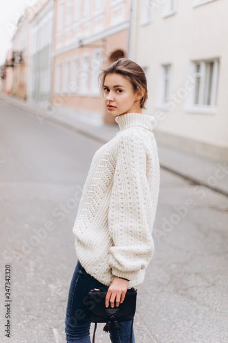 Portrait of young tender redhead young girl with healthy freckled skin wearing knitted scarf looking at camera with serious,pensive expression. Caucasian teen model with ginger hair posing outdoors