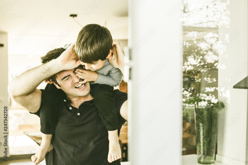 Father playing with his son on his shoulders at home. Love and happiness between child and father