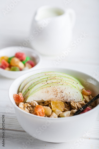 Breakfast bowl of oat granola with apple and dry fruit in a white bowl on white wooden background with a yogurt. Copy space