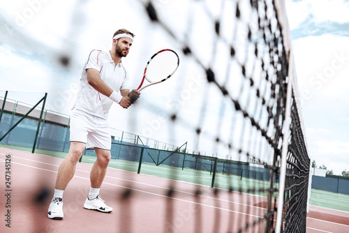 Tennis player is getting ready for the game. Handsome tennis player is standing on the court, near the net, ready for the shot © Friends Stock
