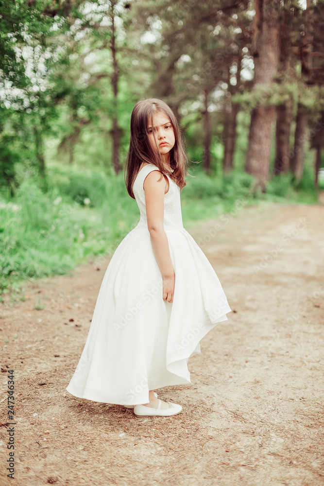 Outdoor portrait of cute brunette emotional girl dancing and having fun in elegant fashionable dress. Childhood, nature, fashion concept