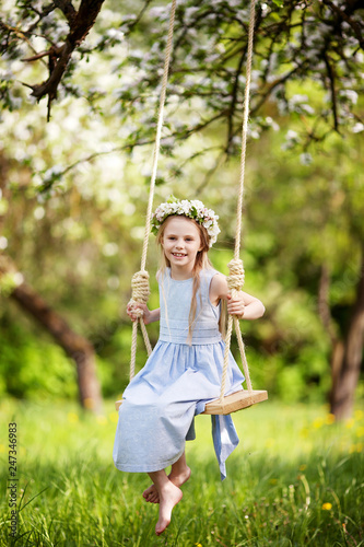Cute young girl having fun on a swing in blossoming old apple tree garden. Sunny day. Spring outdoor activities for kids