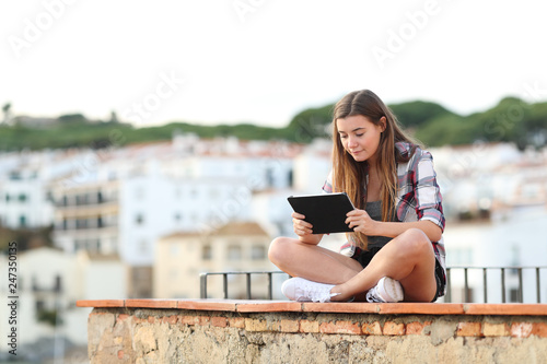 Serious girl using a tablet sitting on a ledge