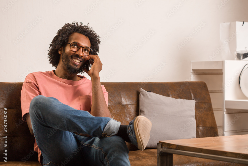 Young african man talking on mobile, sitting on a sofa, he is smiling and positive. Young african man talking on mobile, sitting on a sofa, he is smiling and positive.