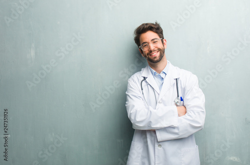 Young friendly doctor man against a grunge wall with a copy space crossing his arms, smiling and happy, being confident and friendly