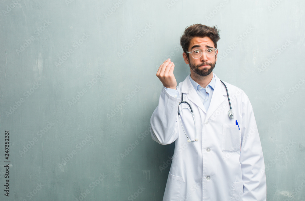 Young friendly doctor man against a grunge wall with a copy space doing a typical italian gesture, smiling and looking straight ahead, symbol or expression with hand, very natural Young friendly doctor man against a grunge wall with a copy space doing a typical italian gesture, smiling and looking straight ahead, symbol or expression with hand, very natural