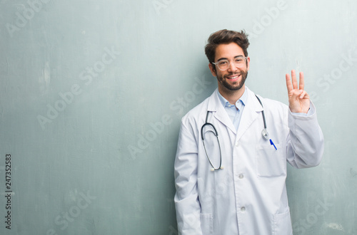 Young friendly doctor man against a grunge wall with a copy space showing number three, symbol of counting, concept of mathematics, confident and cheerful