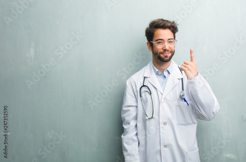 Young friendly doctor man against a grunge wall with a copy space showing number one, symbol of counting, concept of mathematics, confident and cheerful