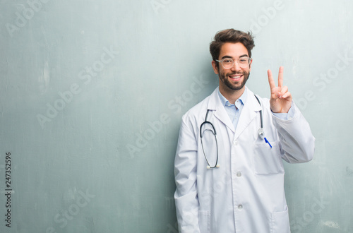 Young friendly doctor man against a grunge wall with a copy space showing number two, symbol of counting, concept of mathematics, confident and cheerful