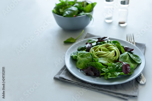 Salad mix with avocado, spinach and beet leaves on gray wooden background. Vegetarian food concept. Selective focus.