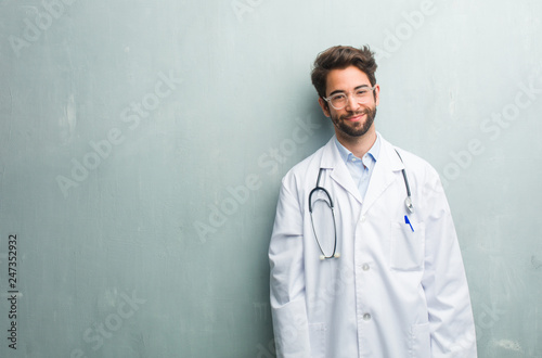 Young friendly doctor man against a grunge wall with a copy space cheerful and with a big smile, confident, friendly and sincere, expressing positivity and success