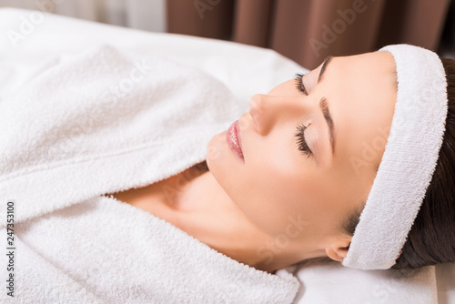 woman lying in white bathrobe and closed eyes at beauty salon