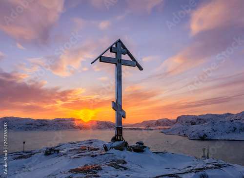 Sun Angel over the mount and Orthodox cross on the top of the snow capped mountain at sunrise. Barents Sea coast at sunrise. Teriberka, Murmansk Region, Kola Peninsula. Russia