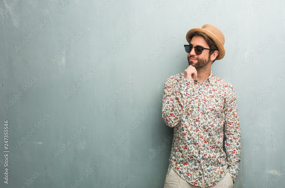 Young traveler man wearing a colorful shirt thinking and looking up, confused about an idea, would be trying to find a solution