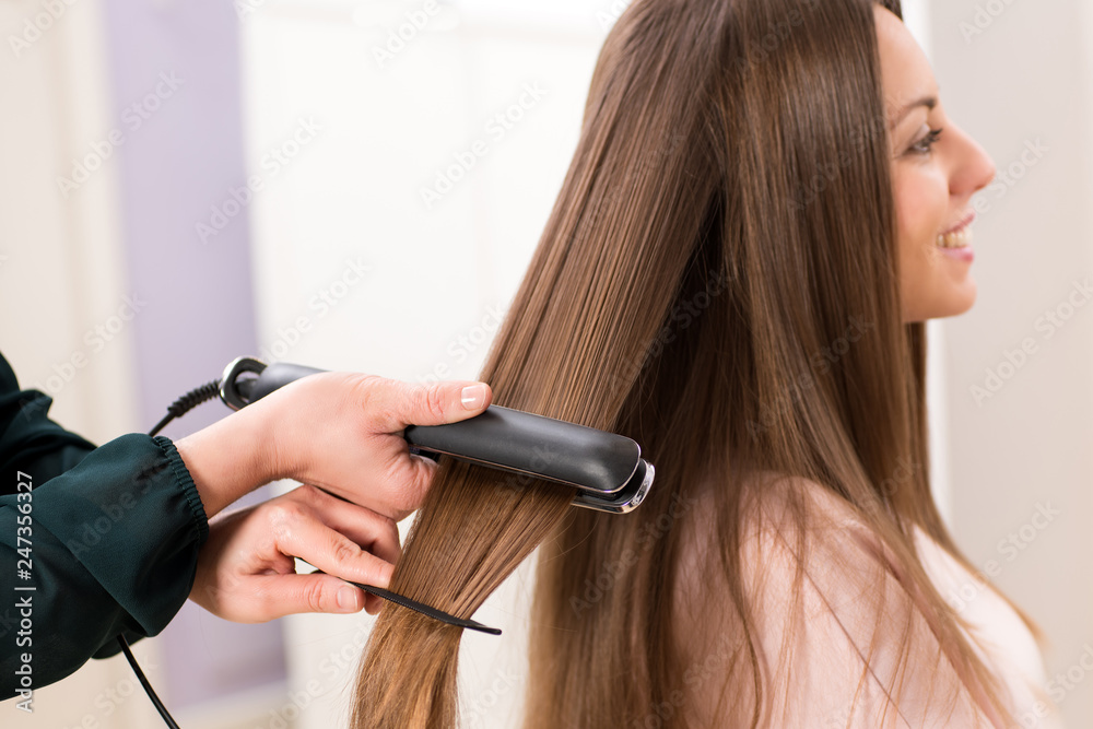 © photology1971 - Hairstylist using a flat iron on long brown hair © photology1971 - Hairstylist using a flat iron on long brown hair