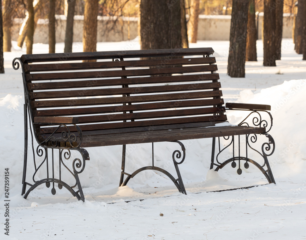 Snow-covered wooden bench in the city park in the morning.