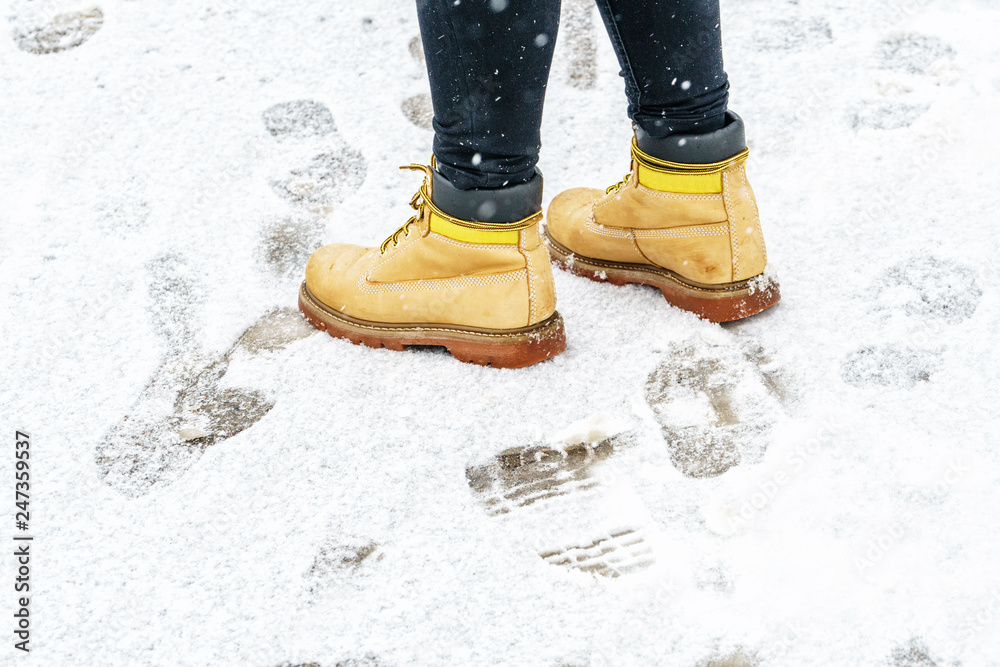 Winter Walk in Yellow Leather Boots. Back view on the feet of a man walking along the icy snowy pavement. Pair of shoe on icy road in winter. Abstract empty blank winter weather background Winter Walk in Yellow Leather Boots. Back view on the feet of a man walking along the icy snowy pavement. Pair of shoe on icy road in winter. Abstract empty blank winter weather background