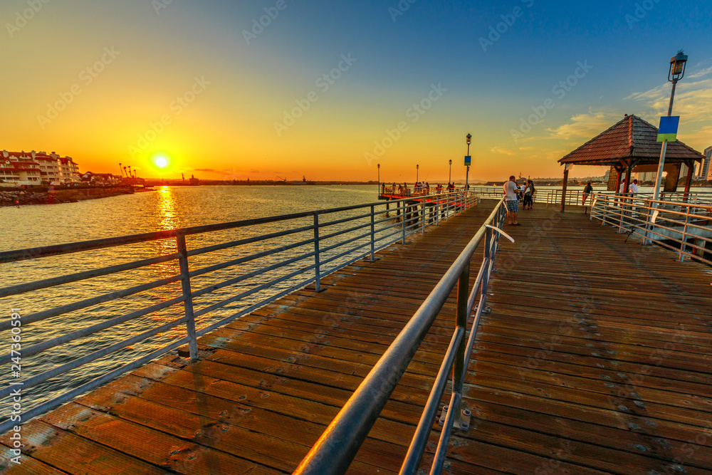 Scenic sunset on San Diego Bay from the old wooden pier in Coronado Island, California. People and tourists fishing and walking and enjoying the view of the San Diego skyline downtown waterfront.
