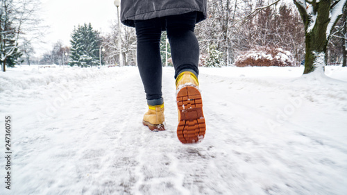 Winter Walk in Yellow Leather Boots. Back view on the feet of a women walking along the icy snowy pavement. Pair of shoe on icy road in winter. Abstract empty blank winter weather background