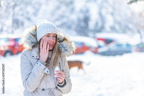 Portrait of a beautiful woman in snow with application of the protective cream in winter. Portrait of a beauty happy lady applying facial moisturizer cream in winter