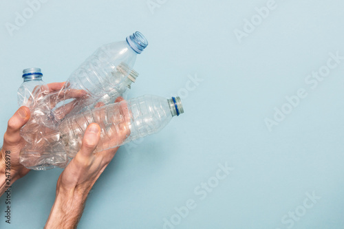 Hand holding empty plastic bottle recycling against a blue background