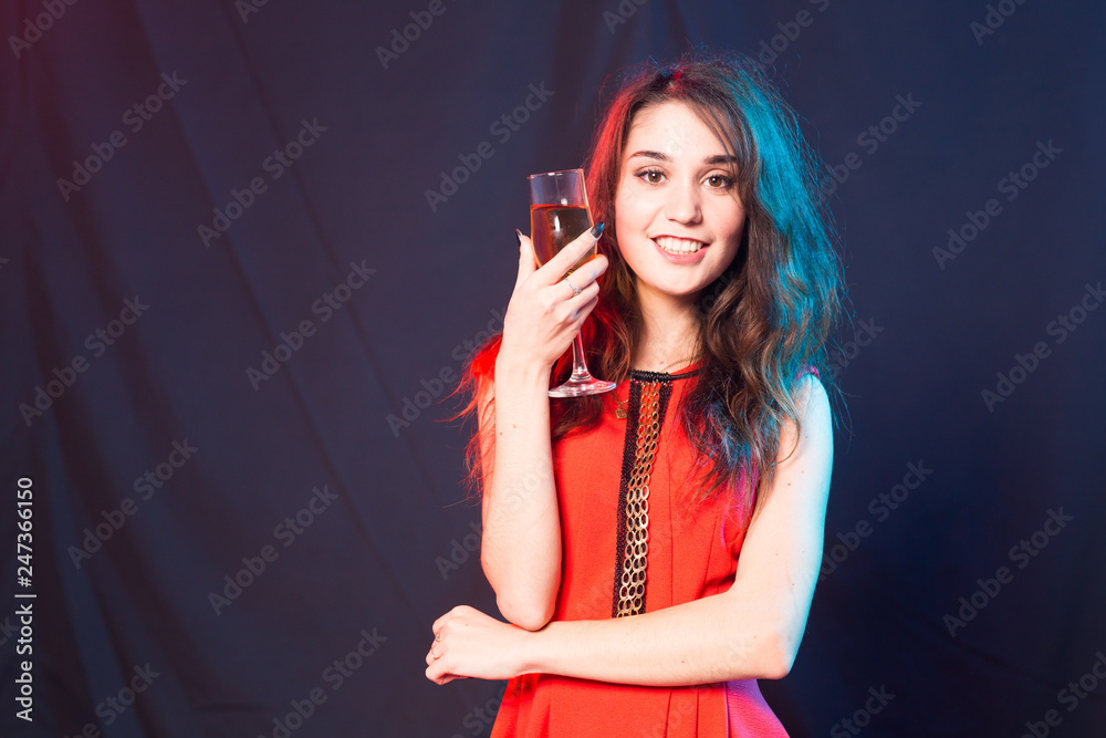 Naklejka premium Alcohol, people and party concept - Young celebrating woman in red dress. Beautiful model hold wine glass on dark background with copy space
