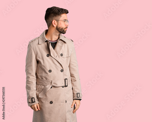 Young man wearing trench coat on the side looking to front