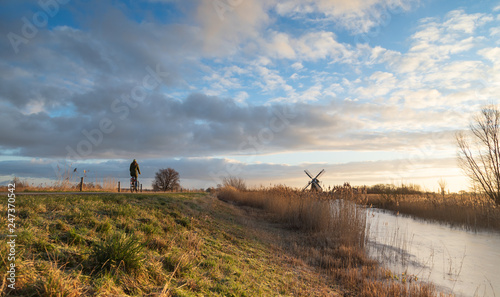 Fotografie Woman cycling in the Dutch countryside near a traditional windmill