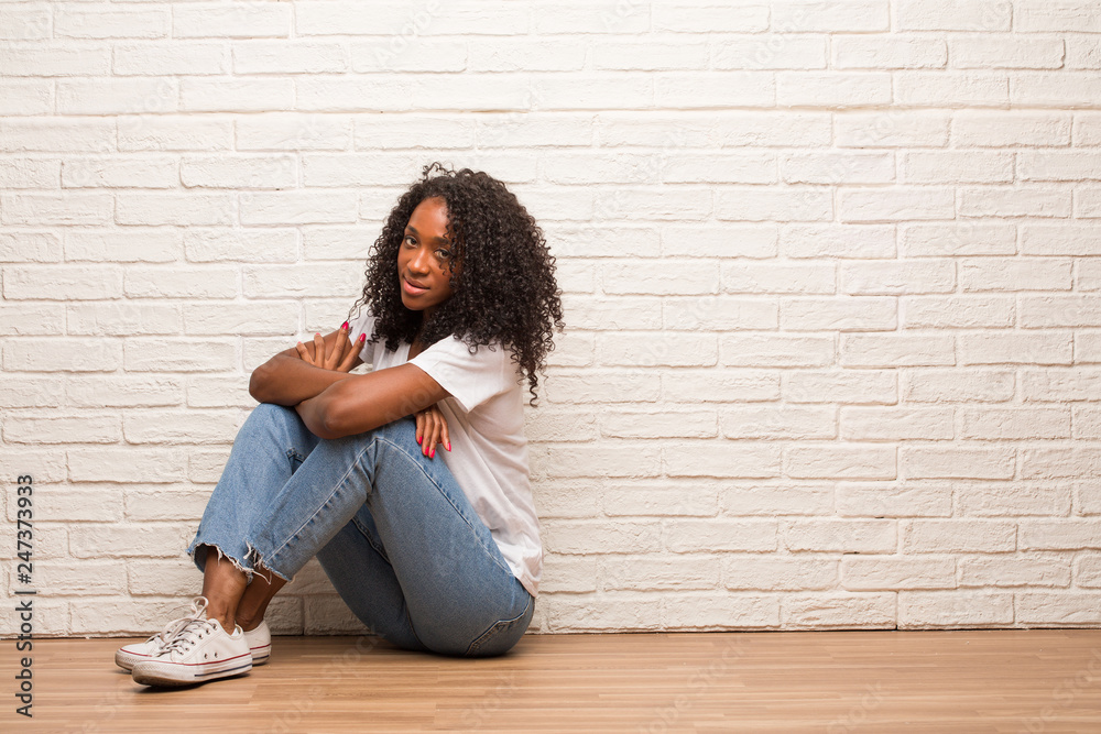 Young black woman sitting on a wooden floor crossing his arms, smiling and happy, being confident and friendly