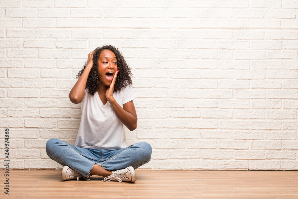 Young black woman sitting on a wooden floor laughing and having fun, being relaxed and cheerful, feels confident and successful Young black woman sitting on a wooden floor laughing and having fun, being relaxed and cheerful, feels confident and successful