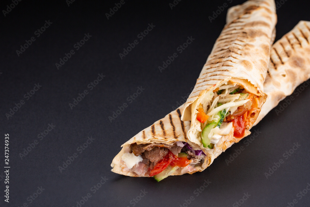 Shawarma sandwich - fresh roll of thin lavash or pita bread filled with grilled meat, mushrooms, cheese, cabbage, carrots, sauce, green. Traditional Eastern snack. On black background. Shawarma sandwich - fresh roll of thin lavash or pita bread filled with grilled meat, mushrooms, cheese, cabbage, carrots, sauce, green. Traditional Eastern snack. On black background.