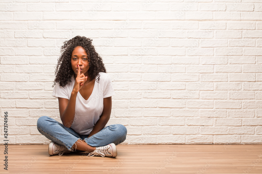 Young black woman sitting on wooden floor keeping a secret or asking for silence, serious face, obedience concept Young black woman sitting on wooden floor keeping a secret or asking for silence, serious face, obedience concept