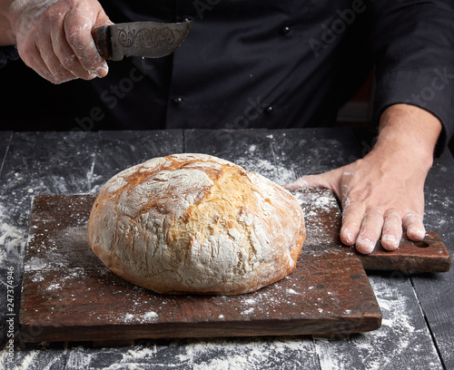 male chef hand holds knife over a whole round baked loaf of bread