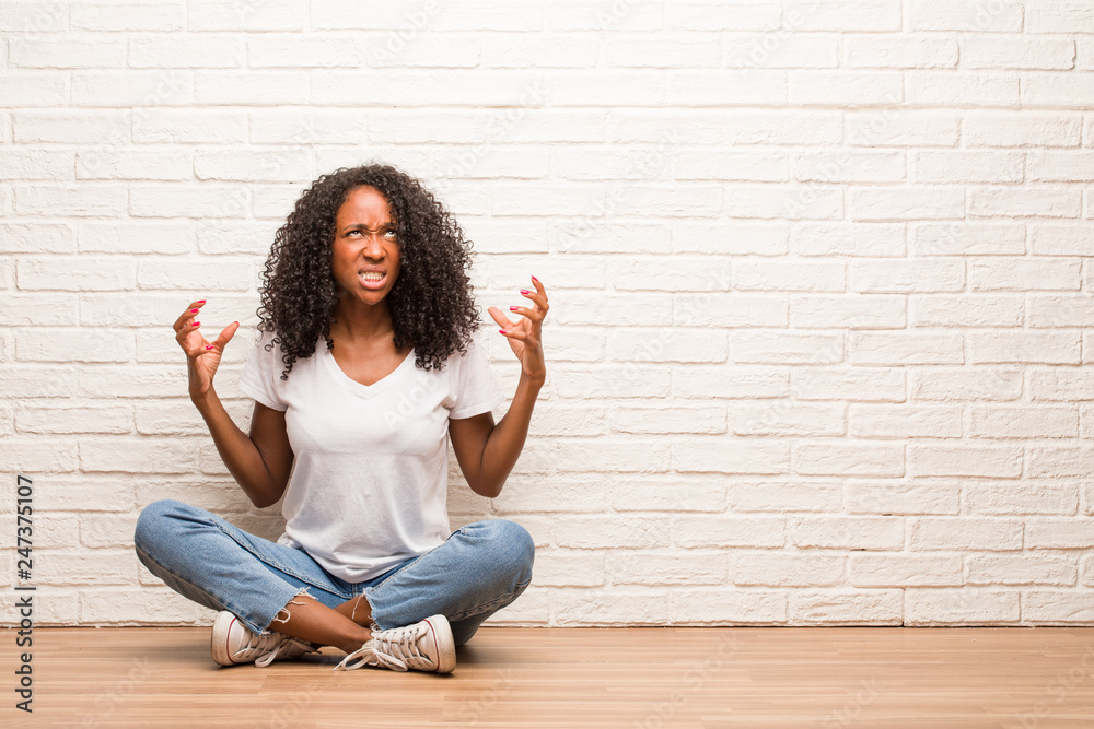 Young black woman sitting on wooden floor very angry and upset, very tense, screaming furious, negative and crazy Young black woman sitting on wooden floor very angry and upset, very tense, screaming furious, negative and crazy