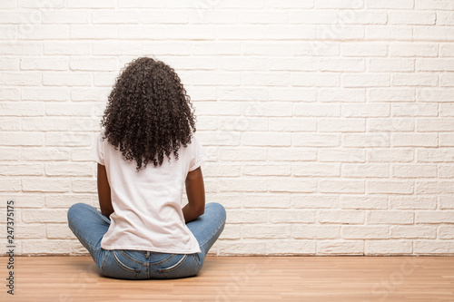 Fotografie Young black woman sitting on wooden floor showing back, posing and waiting, look